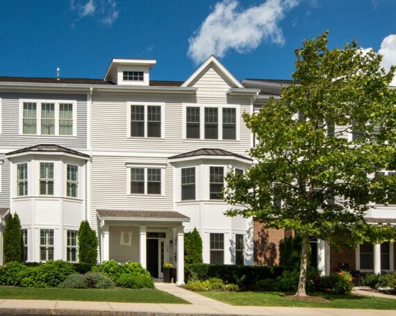 Bright, sunny day on a quiet suburban street in New Jersey, lined with beautiful, well-maintained family homes and green t...