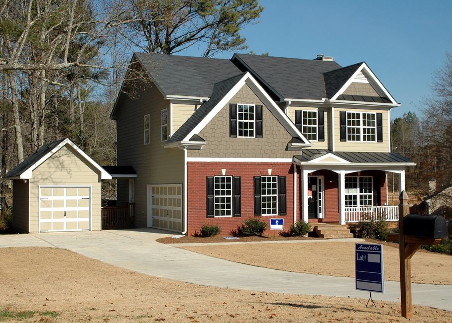 A professional 'For Sale' sign standing on the green front lawn of an attractive, modern suburban home, symbolizing the active but stabilizing New Jersey housing market.