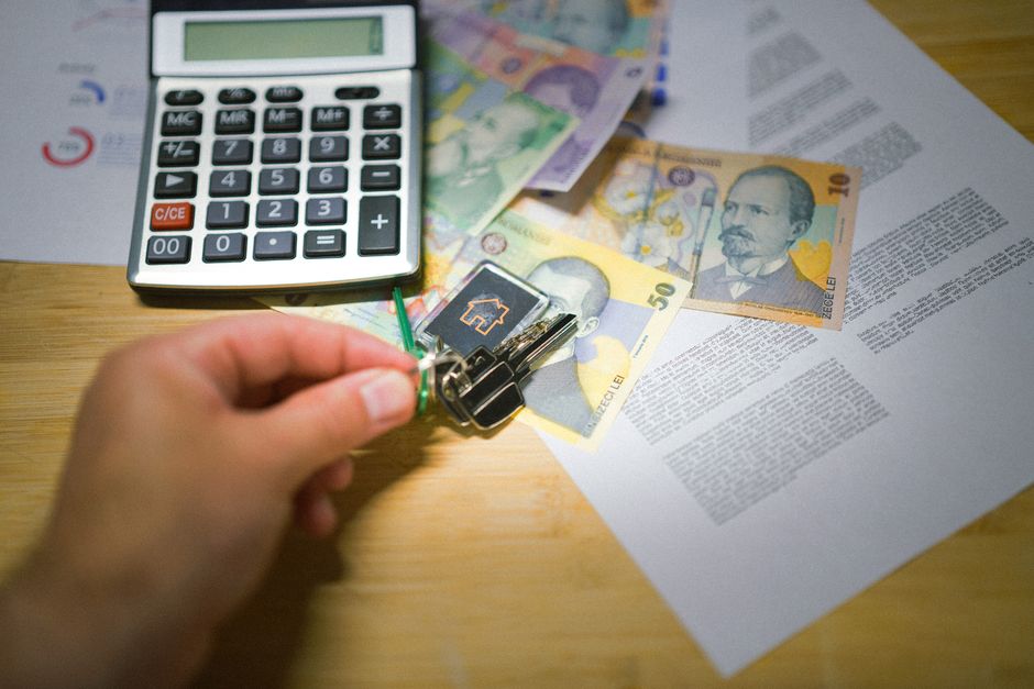 A set of house keys and a calculator on a clean wooden table, symbolizing the financial decisions involved in selling a home for profit.